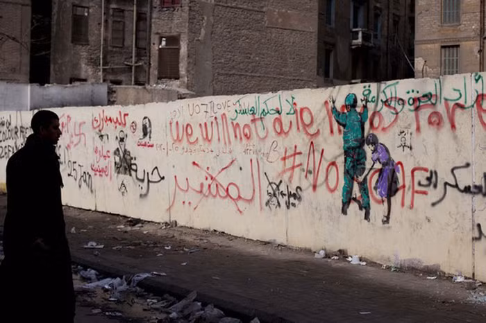 Một người đàn ông đứng nhìn những hình vẽ và chữ viết nguệch ngoạc: “Chúng ta sẽ không bao giờ chết”.