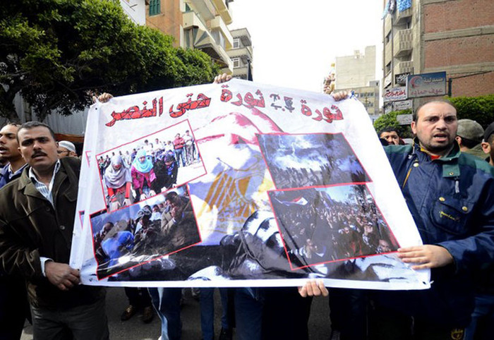 Hai người khác với tấm biểu ngữ có dòng chữ: “Cuộc cách mạng 25/1 sẽ còn tiếp tục cho đến ngày chiến thắng”. Hai người khác với tấm biểu ngữ có dòng chữ: “Cuộc cách mạng 25/1 sẽ còn tiếp tục cho đến ngày chiến thắng”.