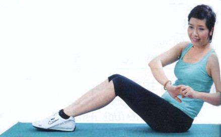 Động tác 2: - Nằm ngửa hơi co gối, bàn chân áp sát mặt sàn, 2 tay để qua đầu tay trái nắm tay phải. - Nâng người lên cao, tay chạm gối. - Sau đó nghiêng sang trái, phải, ngồi thẳng lưng, tay chạm gối, rồi trở về tư thế ban đầu. Giữ cố định phần mông.