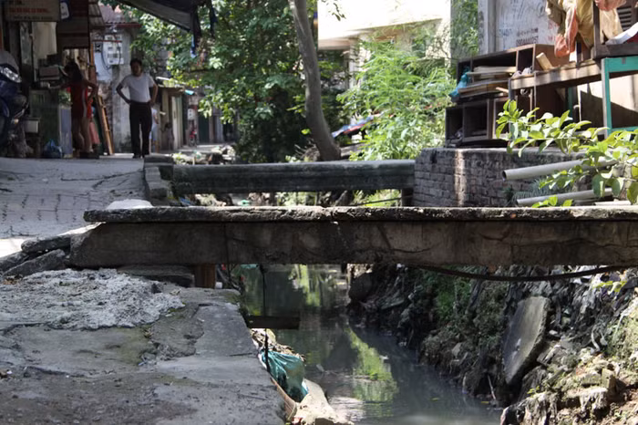 Những chiếc cầu tạm bợ bắc qua con mương đen này được người dân dựng lên để đi tạm trong khi "đợi chờ trong mỏi mòn" dự án cải tạo con mương đen này được thực hiện.