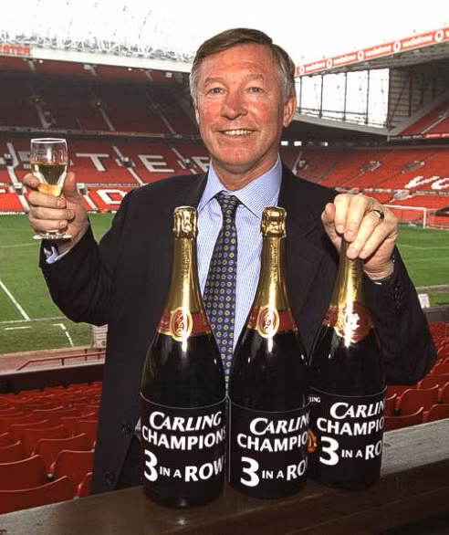 Sir Alex Ferguson bên cạnh 3 chai rượu tượng trưng cho 3 chức vô địch Premier League liên tiếp từ 1999 tới 2001 của Manchester United.