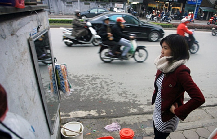 Một bạn gái thử chiếc áo với chiếc gương được treo trên vỉa hè. Một bạn gái thử chiếc áo với chiếc gương được treo trên vỉa hè.