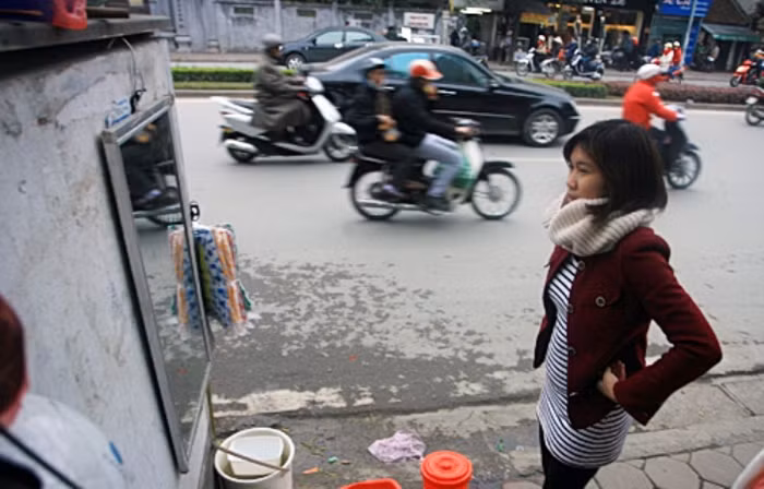 Một bạn gái thử chiếc áo với chiếc gương được treo trên vỉa hè.