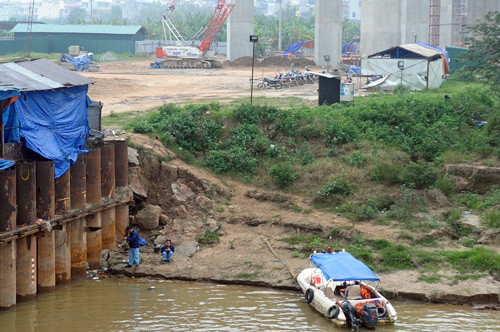 Dưới bờ sông, hai người đàn ông mặc đồng phục đang ngồi câu cá. Theo lời nhân viên bảo vệ, họ là những công nhân thi công tại đây. Dưới bờ sông, hai người đàn ông mặc đồng phục đang ngồi câu cá. Theo lời nhân viên bảo vệ, họ là những công nhân thi công tại đây.