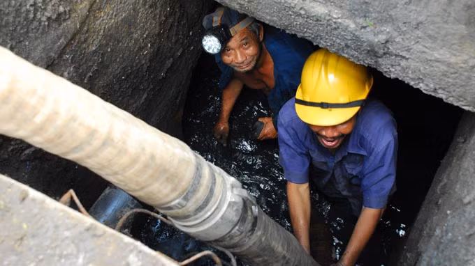 Anh Võ Văn Huệ và Bùi Văn Phước, công nhân Công ty TNHH-MTV Thoát nước đô thị TP.HCM - đơn vị mà giám đốc nhận lương 2,6 tỉ đồng/năm, nạo vét hệ thống cống trên đường Nguyễn Hữu Cảnh, Q.Bình Thạnh. Các anh cho biết tiền lương của mình hiện nay là 8 triệu đồng/tháng - Ảnh: Hoàng Thạch Vân