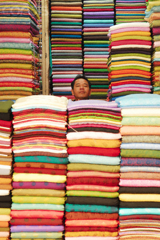 Một người đàn ông như "biến mất" giữa những chồng vải cao có màu sắc rực rỡ. Một người đàn ông như "biến mất" giữa những chồng vải cao có màu sắc rực rỡ.