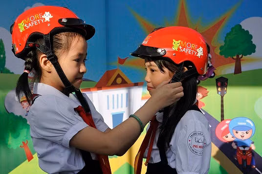 Các em học sinh tiểu học đội mũ bảo hiểm do YMVN trao tặng.