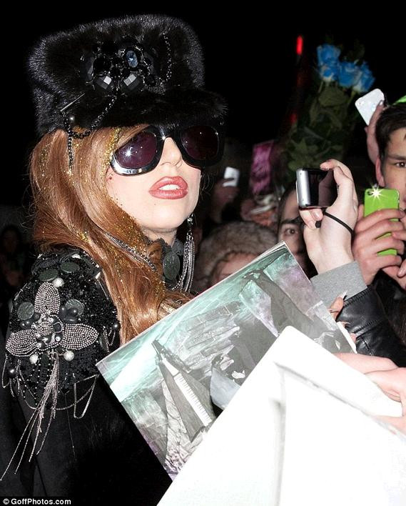 Đầu đội chiếc mũ lông đen đính đá và trang sức đen, mặt đeo kính râm đen, chiếc áo bó sát người màu đen đính đá để hở lưng. Đầu đội chiếc mũ lông đen đính đá và trang sức đen, mặt đeo kính râm đen, chiếc áo bó sát người màu đen đính đá để hở lưng.