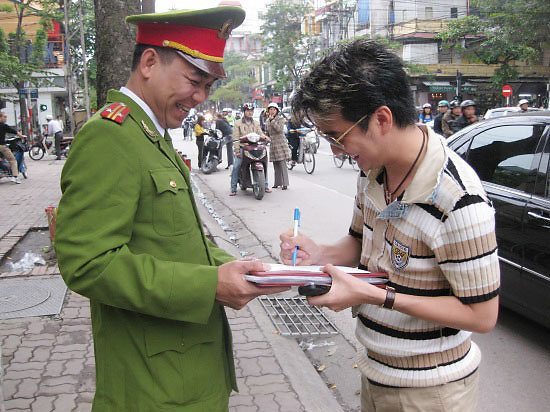 Mr Đàm ký tặng chiến sĩ công an. Từ xa, một đôi nam nữ tò mò đứng nhìn. Mr Đàm ký tặng chiến sĩ công an. Từ xa, một đôi nam nữ tò mò đứng nhìn.