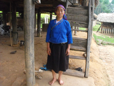 Người đàn bà Nùng với đôi chân trần đứng trước cầu thang căn nhà sàn ọp ẹp.