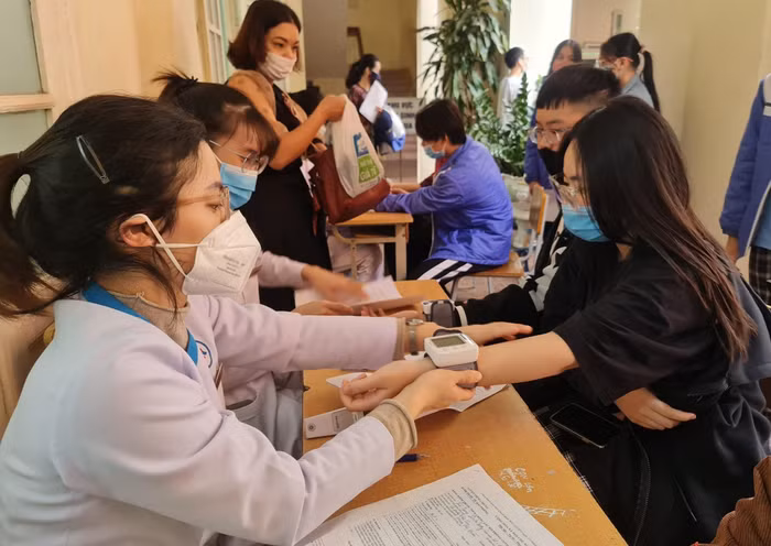 Học sinh nhà trường được chia ca tiêm theo từng lớp. Sau khi hoàn thành các bước khám sàng lọc, tiêm, học sinh được phát sữa, bánh để tăng cường sức khoẻ và được theo dõi 30 phút. Phụ huynh học sinh, giáo viên và đoàn thanh niên của trường động viên, hỗ trợ học sinh tại khu vực theo dõi sau tiêm (Ảnh: Lã Tiến)