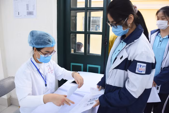 Nhân viên y tế kiểm tra danh sách học sinh đăng ký tiêm (Ảnh: NH)