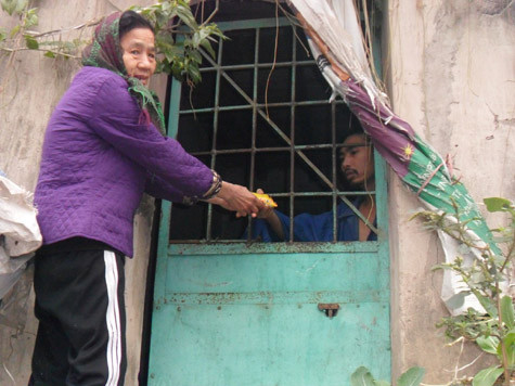 Bà Na đang luồn bánh mì qua song sắt cho người con điên dại. Bà Na đang luồn bánh mì qua song sắt cho người con điên dại.