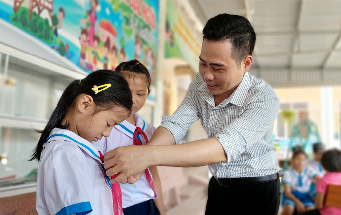 Thầy giáo Tổng phụ trách Đội Nguyễn Văn Bình hướng dẫn học sinh thắt khăn quàng đỏ (Ảnh: Lã Tiến)