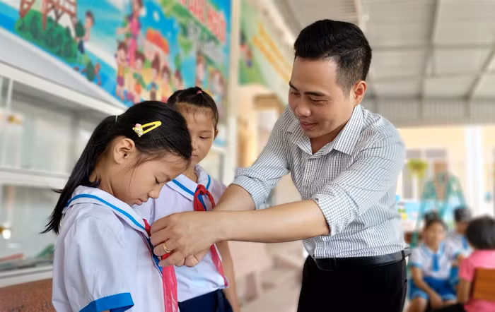 Thầy giáo Tổng phụ trách Đội Nguyễn Văn Bình hướng dẫn học sinh thắt khăn quàng đỏ (Ảnh: Lã Tiến)