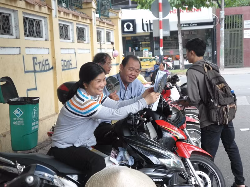 Trời nóng nực, tay phải cầm quạt giấy nhưng bà mẹ này khá vui vẻ và tự tin con mình làm bài tốt.