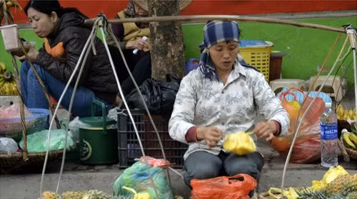 Người phụ nữ này đang gói ghém trái cây bên gánh hàng rong của mình trên phố phường Hà Nội. Người phụ nữ này đang gói ghém trái cây bên gánh hàng rong của mình trên phố phường Hà Nội.