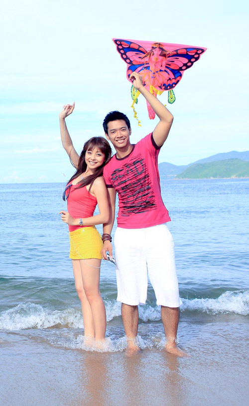 Jennifer Phạm trẻ trung và khỏe khoắn trong trang phục đi biển: Áo thun ba lỗ màu hồng, kết hợp cùng quần short màu vàng rực rỡ. Trên phông nền là mảng xanh bao la của biển cả, Jennifer nổi bật với sắc màu ngày hè của mình.