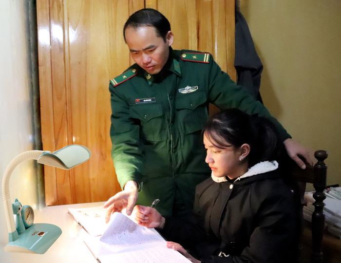 Thiếu tá Ma Đức Minh - Chính trị viên Đồn Biên phòng Phó Bảng hướng dẫn cô con gái út Vàng Thị Chở làm bài tập. Ảnh: Vương Anh. Thiếu tá Ma Đức Minh - Chính trị viên Đồn Biên phòng Phó Bảng hướng dẫn cô con gái út Vàng Thị Chở làm bài tập. Ảnh: Vương Anh.