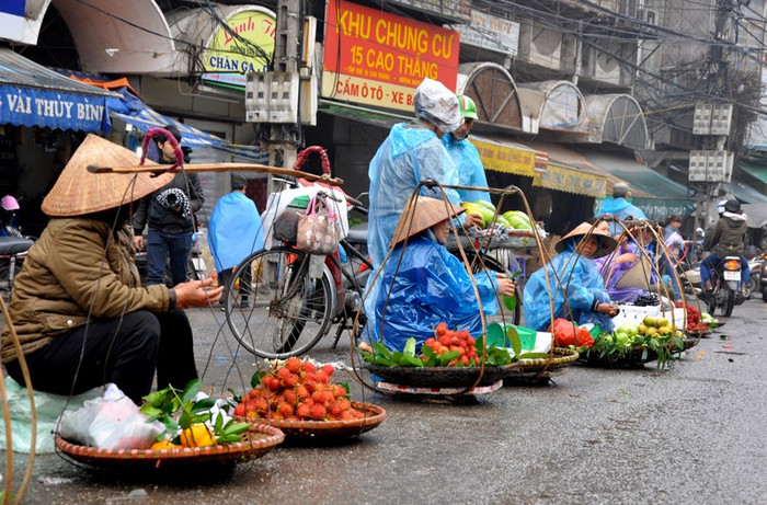 Dù trời có mưa nhưng quanh chợ Đồng Xuân nhiều gánh hàng rong vẫn ngồi ngoài đường để mong bán được hàng. Cái nón, manh áo mưa… là vật dụng để họ chống lại thời tiết khắc nhiệt mỗi ngày.