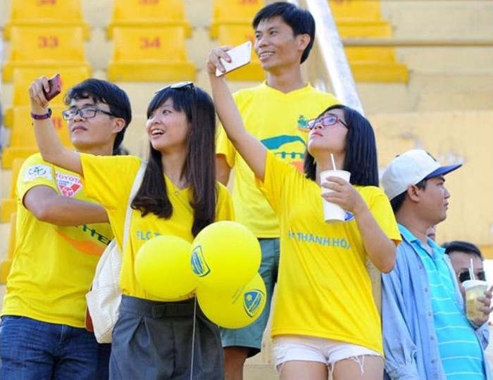 CĐV nữ nhí nhảnh selfie trên khán đài trước trận đấu.