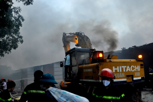 Do ngọn lửa bốc cháy quá lớn, lực lượng PCCC phải huy động xe cẩu để múc phá các tấm tôn bao quanh kho hàng.
