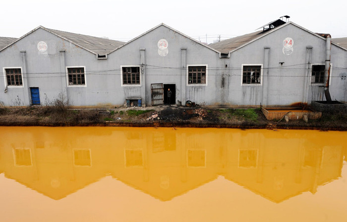 10. Người công nhân trông giống như một nhiếp ảnh gia đứng trước cửa nhà máy sản xuất ốc vít và đinh ốc nằm ngay cạnh con sông bị ô nhiễm tại Jiaxing thuộc tỉnh Chiết Giang, Trung Quốc ( 15/3/2012). Việc Trung Quốc vẫn tiếp tục phụ thuôc vào ngành công nghiệp nặng cũng đồng nghĩa nước này sẽ không thể thực hiện thành công mục tiêu làm sạch không khí và nước đề ra trong năm 2011.