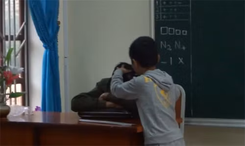Cảnh thầy Nguyễn Như Tưởng, giáo viên dạy môn Thủ Công tại lớp 2A trong giờ học gục trên bàn được một nam sinh lên thoa dầu, nhổ tóc bạc (Ảnh cắt từ clip)