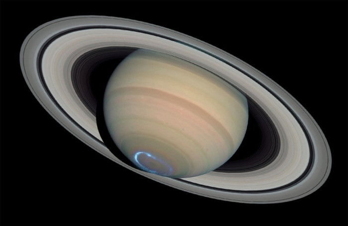 12. Ánh sáng nhảy múa của cực quang trên sao Thổ. Nhìn từ không gian, một cực quang xuất hiện như một chiếc nhẫn khí phát sáng bao quanh vùng cực của sao Thổ. Cực quang xuất hiện khi các hạt tích điện trong không gian va chạm vào từ trường của hành tinh. Các hạt tích điện tăng gia tốc lên mức năng lượng cao sau đó tạo thành dòng trong bầu khí quyển phía trên. Nhiều lần va chạm với các chất khí trong bầu khí quyển của hành tinh đã tạo ra những tia năng lượng sáng dưới dạng có thể nhìn thấy, tia cực tím và tia hồng ngoại. Các nhà thiên văn đã kết hợp hình ảnh tia cực tím của khu cực Nam của sao Thổ với vùng ánh sáng nhìn thấy trên hành tinh cùng với những vòng tròn đồng tâm thu được từ cả kính thiên văn Hubble và tàu vũ trụ Cassini để tạo lên bức ảnh này.