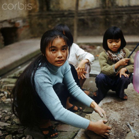 Một cô bé chơi đất sét trên sân nhà cùng với các em.