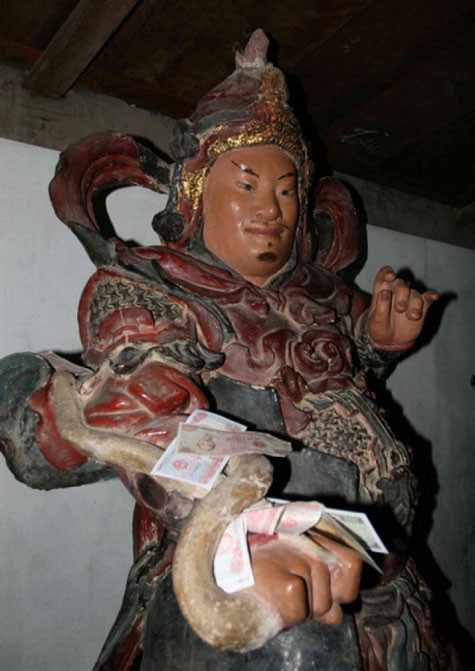 Tiền lẻ được nhét vào các khe trên tay cầm binh khí của tượng La Hán chùa Mía (Sơn Tây, Hà Nội)