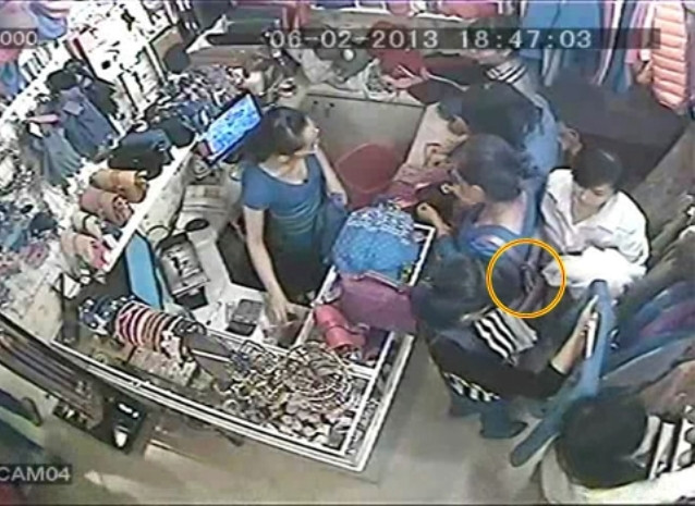 Tên áo đen giơ cao một món hàng để che mắt một người khách khác vừa tiến lại Tên áo đen giơ cao một món hàng để che mắt một người khách khác vừa tiến lại