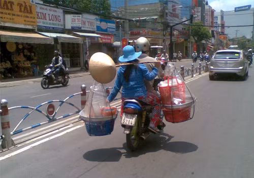 Ngồi xe máy vẫn gánh hàng. Ảnh: Đình Chí.