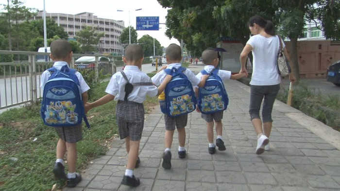 4 cậu bé được mẹ đưa tới lớp, 1 cậu tinh nghịch đeo cặp sách trước ngực 4 cậu bé được mẹ đưa tới lớp, 1 cậu tinh nghịch đeo cặp sách trước ngực