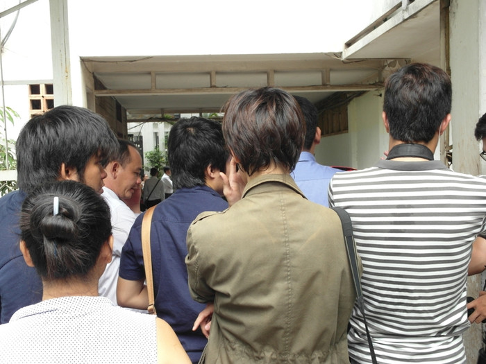 Các phóng viên đang đứng dưới trời nắng, ngay trước cửa vào khu dân cư.