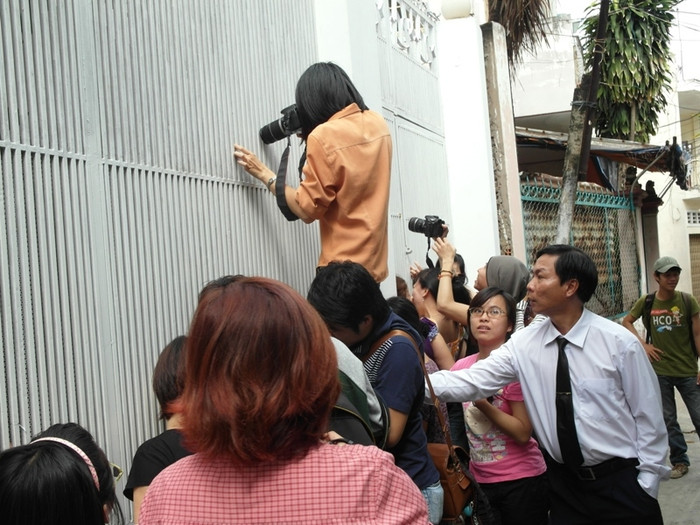 Ra cổng sau, đứng lên vai đồng nghiệp, giơ máy ảnh qua khe hẹp, cố gắng chụp ảnh.