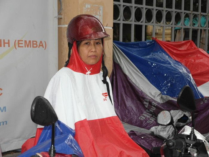 Một bà mẹ ngồi trên xe, mặc áo mưa chờ con thi đại học.