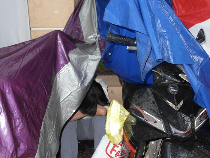 Treo chiếc áo mưa hai bên xe như mái nhà, vị phụ huynh này chui bên dưới ngồi… ngủ.