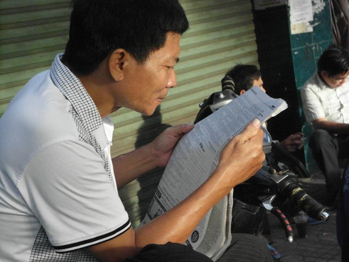 Con vào thi, một phụ huynh chăm chú xem bài giải môn Toán trên báo. Ảnh chụp trước Trường ĐH Sư phạm TP.HCM. Xem đáp án môn Vật lí - Xem đáp án môn Toán - Xem đáp án môn Hóa