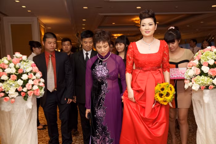 Và cô dâu Thuý Vinh trong tà áo dài cách điệu màu đỏ, tay cầm đoá hoa cúc vàng bước ra.