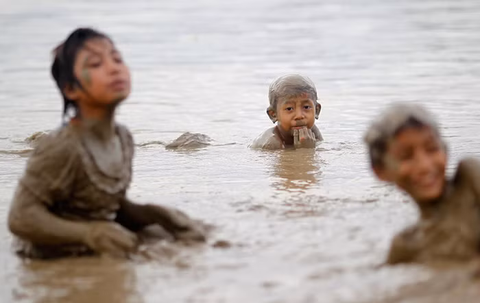 Trẻ em nông thôn chơi đùa trên sông, bùn đất đầy người