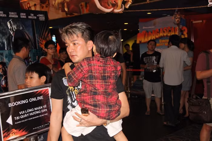 Anh bồng con bước nhanh vào phòng vé, tránh ánh mắt tò mò của mọi người. Trong khi cậu con lớn đang mải mê "khám phá" xung quanh.