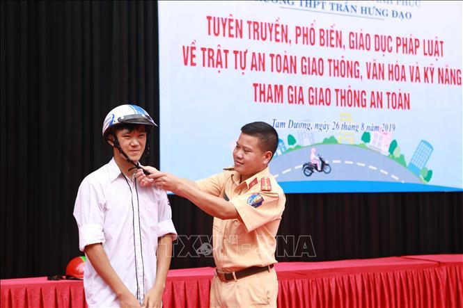 Cán bộ phòng Cảnh sát giao thông, Công an tỉnh Vĩnh Phúc hướng dẫn cài quai mũ bảo hiểm cho học sinh. Ảnh minh họa: TTXVN