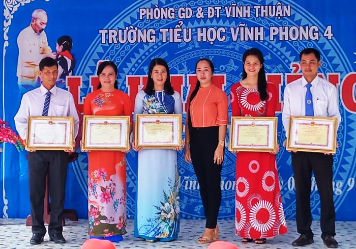 Cô Trịnh Ngọc Thuỳ Mai - Hiệu trưởng Trường Tiểu học Vĩnh Phong 4 (huyện Vĩnh Thuận, tỉnh Kiên Giang, thứ 2 từ trái sang) đã “diễn kịch” nhận giấy chứng nhận tặng thưởng danh hiệu Chiến sĩ thi đua trên lễ đài dù không đạt thành tích này. (Ảnh: c1vinhphong4.vinhthuan.edu.vn). Cô Trịnh Ngọc Thuỳ Mai - Hiệu trưởng Trường Tiểu học Vĩnh Phong 4 (huyện Vĩnh Thuận, tỉnh Kiên Giang, thứ 2 từ trái sang) đã “diễn kịch” nhận giấy chứng nhận tặng thưởng danh hiệu Chiến sĩ thi đua trên lễ đài dù không đạt thành tích này. (Ảnh: c1vinhphong4.vinhthuan.edu.vn).