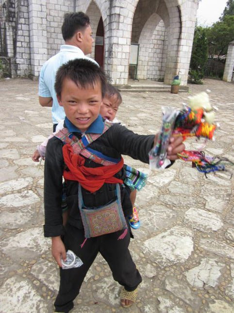 Trên tay mỗi em đều là những món quà lưu niệm nhỏ và sau lưng địu em nhỏ.