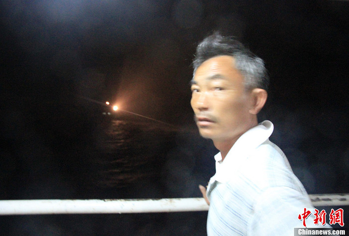 1 ngư dân Trung Quốc chỉ ánh đèn pha của "tàu công vụ nước ngoài" đang áp sát đội hình tàu cá Trung Quốc