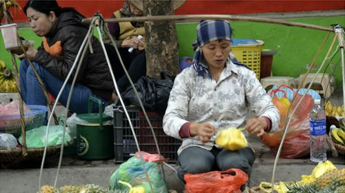 Người phụ nữ này đang gói ghém trái cây bên gánh hàng rong của mình trên phố phường Hà Nội.