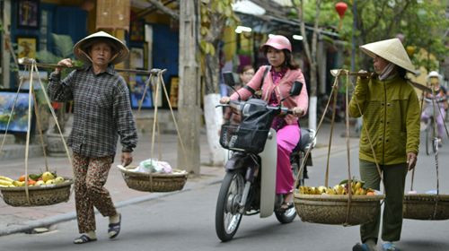 Người gánh hàng, người chạy xe máy trên đường phố Hội An, đoạn gần chiếc cầu Nhật Bản.