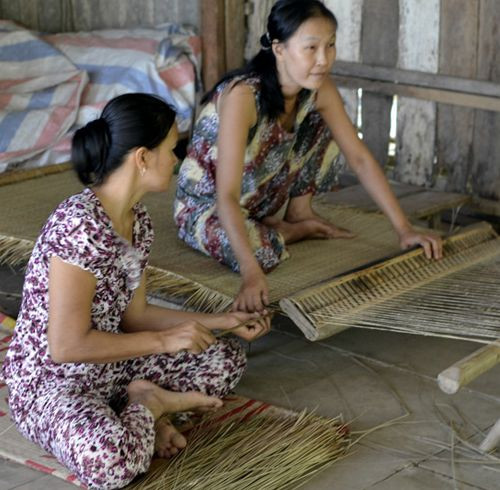 Hai người phụ nữ đan chiếu ở đồng bằng sông Cửu Long, một người giữ khung và đan, còn người kia thì luồn sợi.