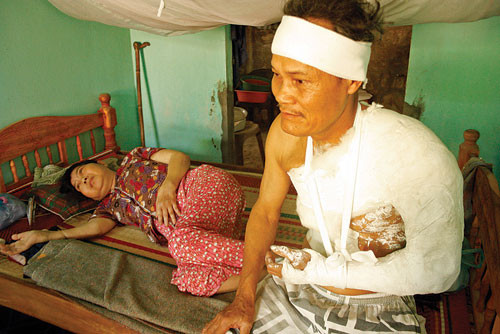 Ông Lê Trọng Kim bị người khai thác cát tấn công gây thương tích nặng, bên cạnh ông là người vợ bị bệnh nằm liệt giường. Ảnh: Gia Tân.